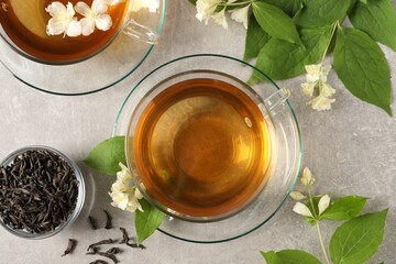 Aromatic jasmine tea in cups, flowers and dry leaves on light grey table, flat lay