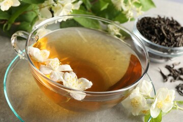Aromatic jasmine tea in cup, flowers and leaves on light grey table, closeup