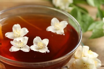 Hot jasmine tea in cup and flowers on wooden table, closeup