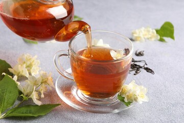Pouring hot jasmine tea into cup on light grey table, closeup