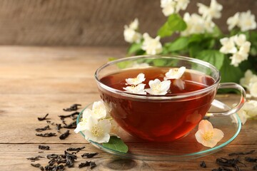 Hot jasmine tea in cup and flowers on wooden table, space for text