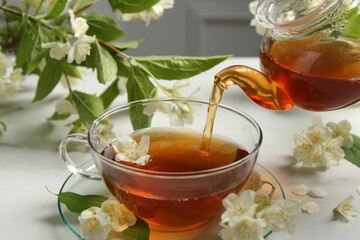 Pouring hot jasmine tea into cup on white marble table, closeup