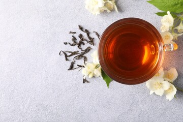 Hot jasmine tea in cup and flowers on light grey table, flat lay. Space for text