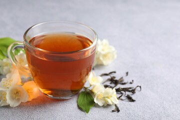 Hot jasmine tea in cup and flowers on light grey table, space for text