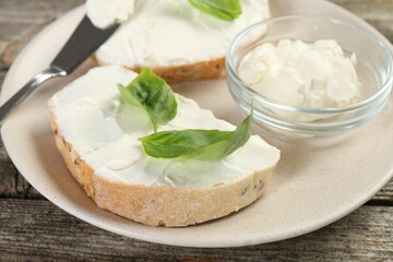Delicious sandwiches with cream cheese and basil leaves on wooden table, closeup