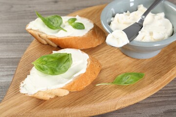 Delicious sandwiches with cream cheese and basil leaves on wooden table, closeup