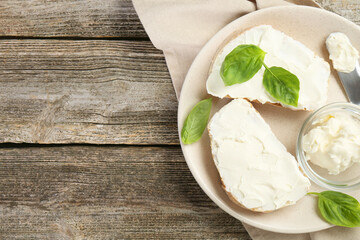 Delicious sandwiches with cream cheese and basil leaves on wooden table, top view. Space for text