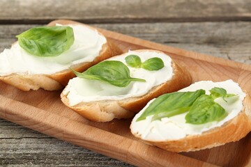 Delicious sandwiches with cream cheese and basil leaves on wooden table, closeup