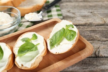 Delicious sandwiches with cream cheese and basil leaves on wooden table, closeup