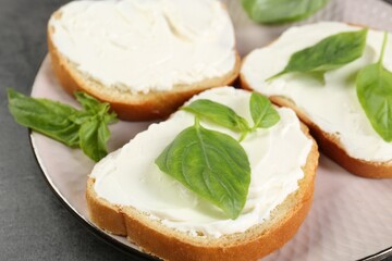 Delicious sandwiches with cream cheese and basil leaves on grey table, closeup