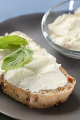 Piece of bread with cream cheese and basil leaves on gray plate, closeup