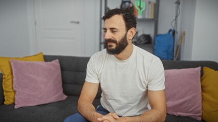 Handsome bearded man sitting on a gray sofa in a modern living room interior.