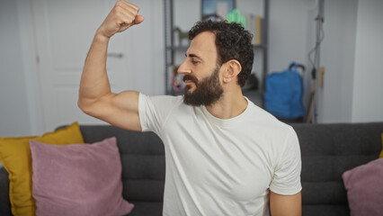 Fototapeta premium Middle-aged man with a beard flexing muscles joyfully inside a modern living room