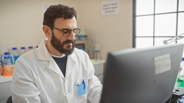 A focused middle-aged man with a beard analyzes data on a computer screen in a laboratory setting.
