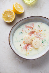 Bowl of scallop and bacon chowder on a light-beige stone background, vertical shot, high angle view