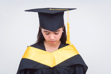 A young woman in a graduation gown and cap looking sad and lonely. The graduate appears to be...