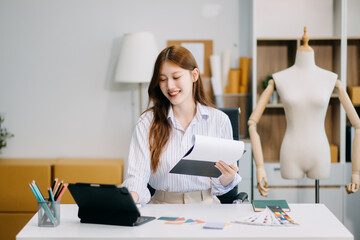 Fashion designer woman talking smart phone and using laptop with digital tablet computer in modern studio