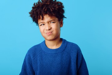 Portrait of a cheerful young african american boy making a playful expression against a bright blue...