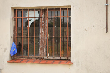 Obraz premium Dirty window showing a small EU flag, countryside. Poverty in Europe.