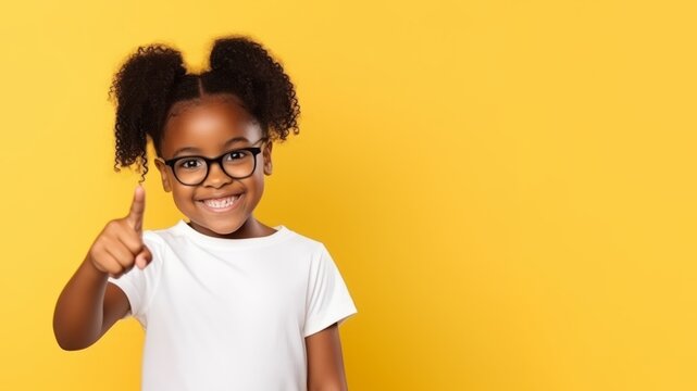 A little girl smile points with her finger to the side on yellow background