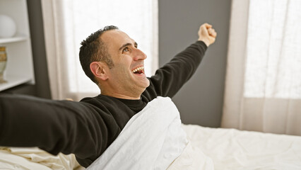 Happy man stretching in bed with a joyous expression in a bright bedroom interior at home