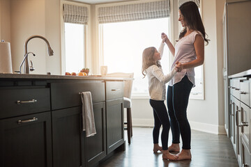 Mother, daughter and dancing in kitchen, happiness and love in house, care and feet of kid on mom. Home, fun and smile for bonding in apartment, teaching and morning for support and holding hands