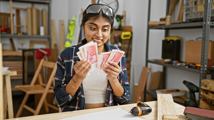 Smiling south asian woman holding icelandic currency in a woodworking workshop.