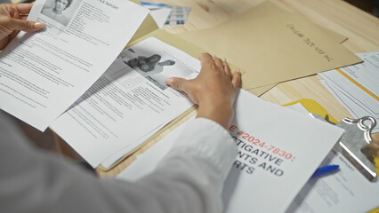 A black woman reviews case files at a cluttered police department desk, portraying a sense of...