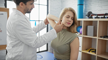 Obraz premium A man doctor examines the shoulder of a woman patient in a therapy room at a clinic.