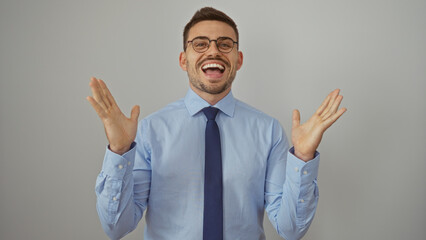 A handsome young hispanic man wearing glasses and a blue dress shirt with a tie smiles enthusiastically over an isolated white background.