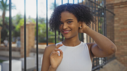 A beautiful young african american woman with curly hair and wearing a white top smiles confidently...