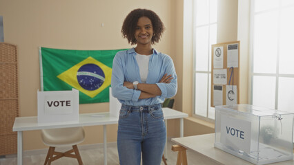 A beautiful young african american woman in an electoral college room stands confidently with arms crossed, brazilian flag in the background, and voting materials on display.
