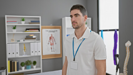 Handsome hispanic man wearing a lanyard standing thoughtfully in a clinic interior near a bookshelf. © Krakenimages.com