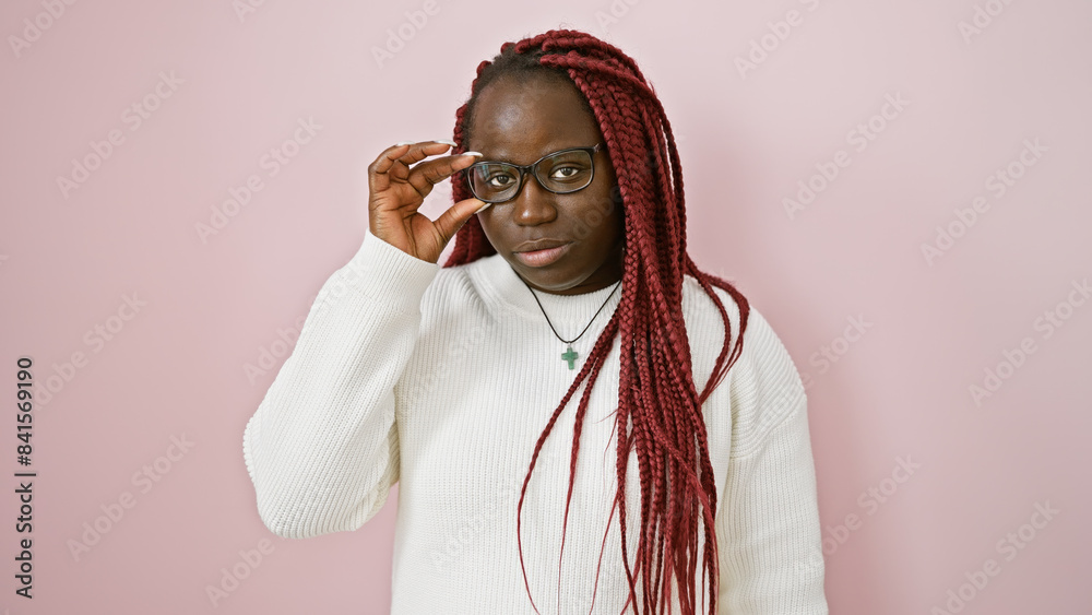 Canvas Prints A confident african american woman with braids adjusts her glasses against a pink background, emulating elegance and poise.