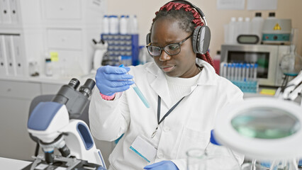African american woman scientist analyzing a sample in a laboratory setting, wearing a white coat and headphones.