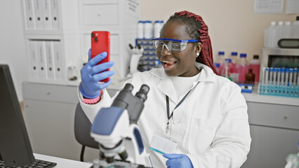 African female scientist conducting a video call on her phone in a laboratory setting.