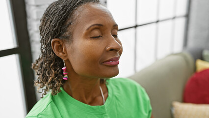 African american woman smiling indoors with closed eyes, wearing earrings and a green shirt...