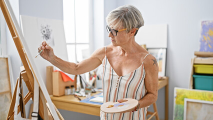 A mature woman artist paints in a bright studio, showcasing creativity and elegance.
