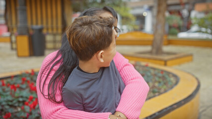 A mother and son enjoy a quiet moment together amidst the bustling city park, surrounded by nature's colors.