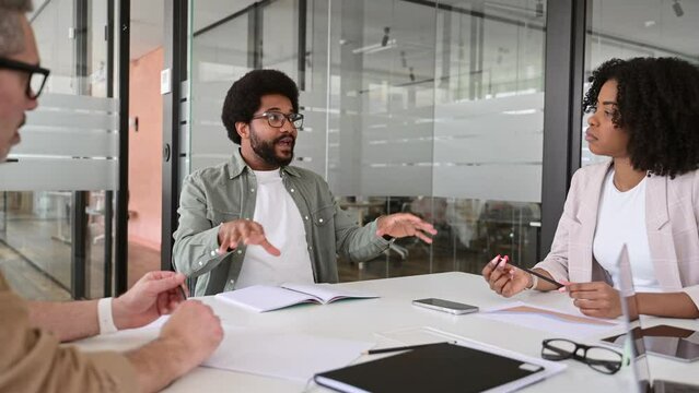 A lively brainstorming session where three colleagues discuss ideas and strategies in a contemporary office setting. The transparent glass walls highlight a collaborative and open work culture
