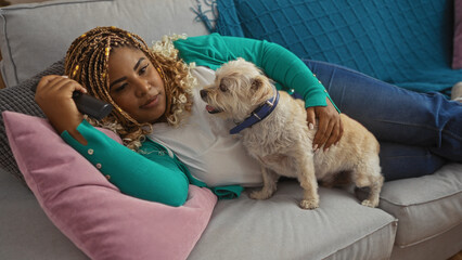 Young african american woman with braids relaxing in a living room with her pet dog on a sofa indoors.