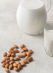Alternative milk of almonds in a glass and glass jug on a wooden background. copy space
