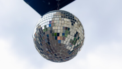 Selective focus of round and sparkle disco ball hanging outdoor in daytime with white cloud as background, Festive decoration glitter silver crystal ball, Party and celebration concept.