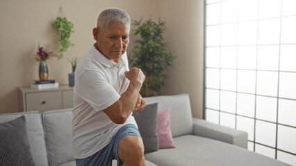 Mature hispanic man exercising in a modern living room, exemplifying healthy aging and an active lifestyle.