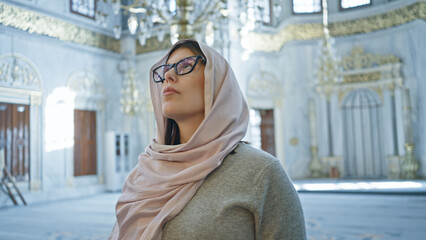 Contemplative woman wearing hijab inside historic istanbul mosque admiring islamic architecture.