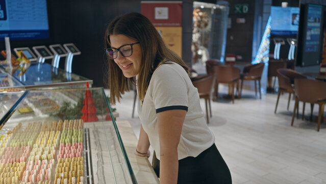 Smiling woman browsing colorful macarons at a modern bakery cafe interior