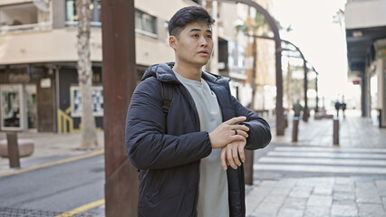 Young asian man wearing a jacket standing on a city street with buildings in the background