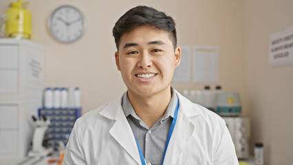 Young asian male scientist in a laboratory setting, smiling at the camera, clad in a lab coat and lanyard. © Krakenimages.com