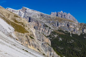 Dolomites beautiful alpine rock tower summits under blue sky in summer. Italian Alps mountains scenic landscape of rocky climbing walls in the high altitude majestic view of the cliff and green valley