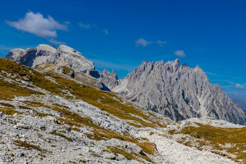 Dolomites beautiful alpine rock tower summits under blue sky in summer. Italian Alps mountains scenic landscape of rocky climbing walls in the high altitude majestic view of the cliff and green valley